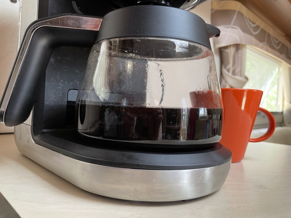 Kahvinkeittimen pannussa kahvia, takana pilkottaa oranssi kahvikuppi.