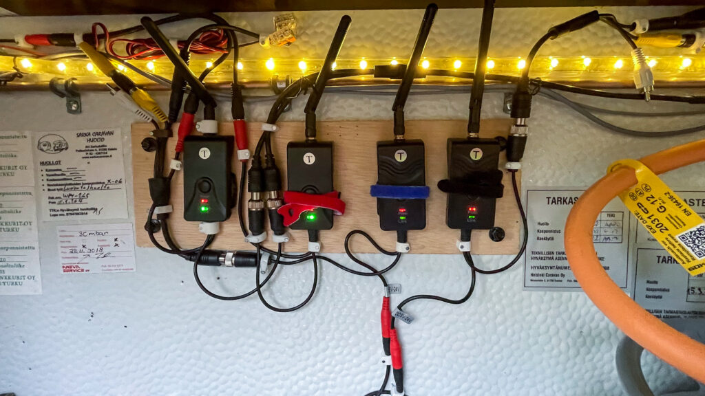 Asuntovaunun kaasupullokotelon takaseinään asennettu rinnakkain neljä digitaalista lähetintä. Kaasupullokotelon valaistus on päällä ja lähettimissä on virrat ja yhteydet.