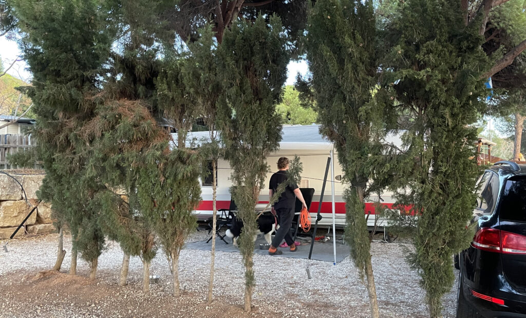Camping Cabopino, asuntovaunu etualalla olevien sypressien takana.